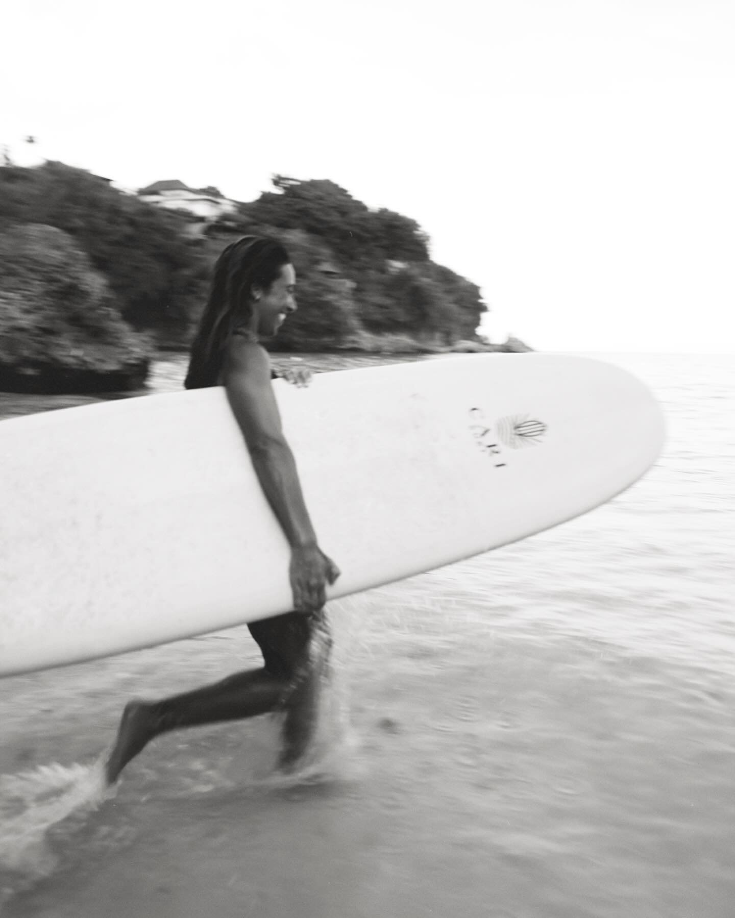 Blurry moody artsy shot of Woman going surfing with Cari Surf logo surfboard