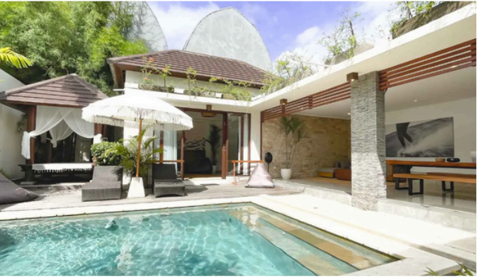 open space villa bedroom onlooking the pool with white retro style umbrella in cari surf camp Bali resort in Indonesia.